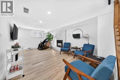 Finished basement featuring wood-finish flooring, a white brick fireplace, recessed lighting, and a visible window - 19 Glen Forest Drive, Hamilton, ON 