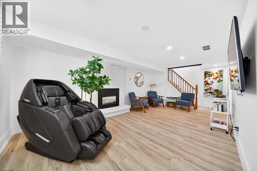 Spacious room featuring light wood-finish flooring, a white brick fireplace with a dark insert, recessed lighting, and a wood staircase with balusters - 19 Glen Forest Drive, Hamilton, ON 