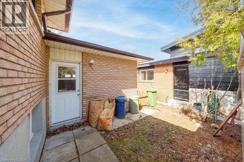 Brick exterior with a white entry door, an exterior wall light, and a concrete paver pathway - 19 Glen Forest Drive, Hamilton, ON 