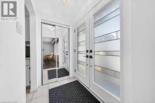 Entryway featuring dual frosted glass panel doors with dark hardware, mirrored closet doors, and light-toned floor tiling - 19 Glen Forest Drive, Hamilton, ON 