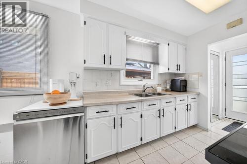 Kitchen featuring white cabinetry, light-toned countertops, a double basin sink, and tile flooring - 19 Glen Forest Drive, Hamilton, ON 