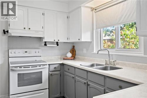 Kitchen featuring two-tone cabinetry with white upper cabinets and grey lower cabinets, a dual basin stainless steel sink with a chrome faucet, light-toned countertops, and a white electric range with - 1083 Melton Drive, Mississauga, ON 