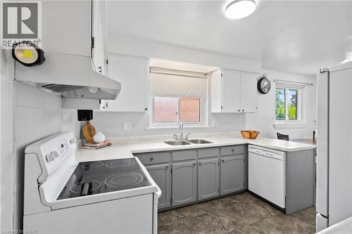 Kitchen featuring a dual-tone cabinetry with white upper cabinets and gray lower cabinets, a white electric range with a hood fan, a double basin stainless steel sink, a white dishwasher, and durable - 1083 Melton Drive, Mississauga, ON 