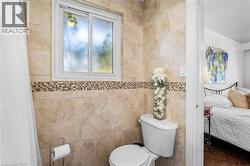 Tiled bathroom featuring a sliding window, a toilet, and a decorative mosaic tile accent - 