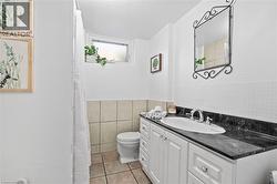 3-piece Basement bathroom featuring a white vanity with a dark countertop, an undermount sink, and a decorative wall mirror - 