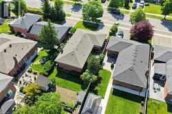 Aerial view showcasing an L-shaped brick residence with a dark shingle roof, a paved driveway, and established front and rear landscaping - 