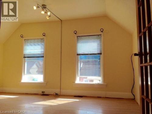 Room featuring wood-finish flooring, two large windows with blinds, a multi-spot track lighting fixture, and a dark wood-paneled door - 269 Cannon Street E, Hamilton, ON 