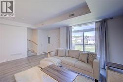 Spacious living area featuring wood-finish flooring, a large window with exterior scenery, recessed lighting, and a staircase with a natural wood handrail - 