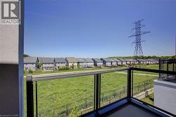Balcony featuring glass panel railing and a painted exterior wall, overlooking a green expanse and residential properties - 