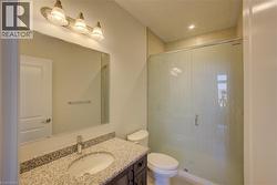 Bathroom featuring a glass-enclosed shower, a vanity with a granite countertop, an undermount sink, and a wall-mounted light fixture - 