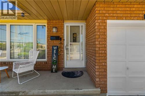 Brick exterior featuring a concrete porch, large front windows, an exterior light fixture, a black mailbox, and a paneled garage door - 102 Juniper Drive, Hamilton, ON 