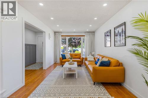 Bright living space featuring recessed lighting, wood-finish flooring, a large picture window, and a paneled accent wall in the adjacent entry - 102 Juniper Drive, Hamilton, ON 