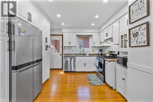 Well-appointed kitchen featuring wood-finish flooring, white cabinetry with dark hardware, stainless steel appliances, recessed lighting, and a window above the sink - 102 Juniper Drive, Hamilton, ON 