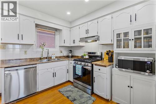 Kitchen featuring white cabinetry, stainless steel appliances, wood-finish flooring, a double basin sink, and a tiled backsplash - 102 Juniper Drive, Hamilton, ON 