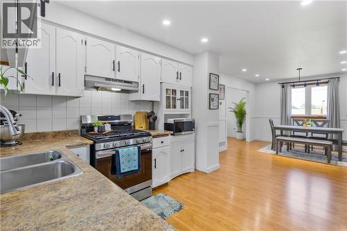 Open-concept kitchen featuring white cabinetry with black hardware, stainless steel appliances, and a double basin sink - 102 Juniper Drive, Hamilton, ON 