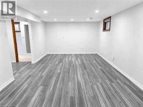 Spacious room featuring wood-finish flooring, recessed lighting, white baseboards, and a window with wood trim - 102 Juniper Drive, Hamilton, ON 