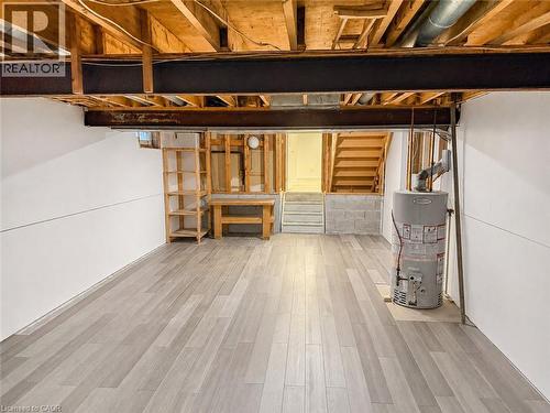 Finished basement area featuring wood-finish flooring, white paneling, exposed ceiling joists, and a partial staircase - 102 Juniper Drive, Hamilton, ON 