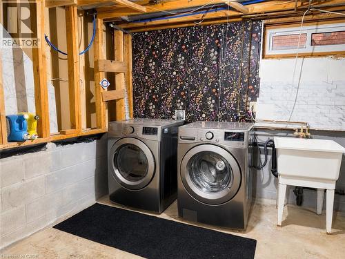 Utility area featuring two front-loading laundry appliances, a white utility sink, exposed wood framing, and concrete block walls - 102 Juniper Drive, Hamilton, ON 