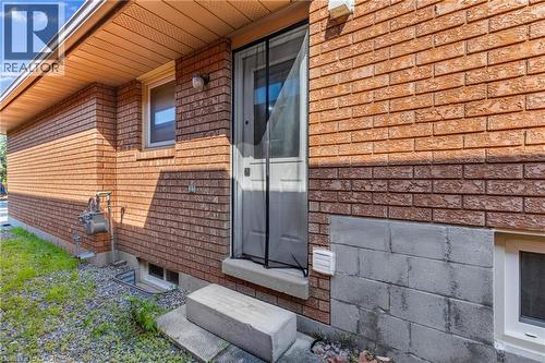 Red brick exterior with a side entry door, concrete steps, and a white window trim - 102 Juniper Drive, Hamilton, ON 