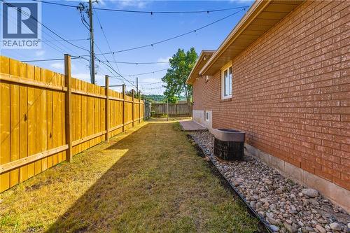 Expansive side yard featuring a new wood privacy fence, brick exterior, and decorative rock landscaping - 102 Juniper Drive, Hamilton, ON 