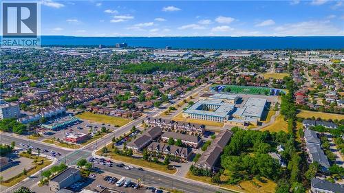 Aerial perspective showcasing a developed community with a prominent institutional building, multiple residential areas, and commercial storefronts - 102 Juniper Drive, Hamilton, ON 
