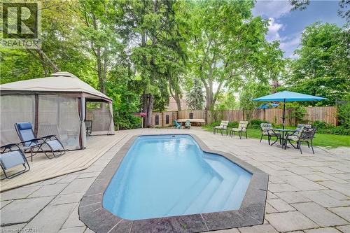In-ground pool surrounded by stone patio with privacy fencing and mature trees - 314 Glasgow Street, Kitchener, ON 