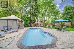 In-ground pool surrounded by stone patio with privacy fencing and mature trees - 