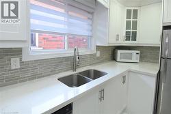 Kitchen featuring a double basin stainless steel sink with a high-arc faucet, quartz countertops, and a full tile backsplash - 