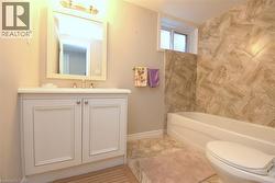 Bathroom featuring a white vanity with panel cabinetry, a rectangular mirror, a bathtub with a tiled surround, and a coordinating tiled floor - 