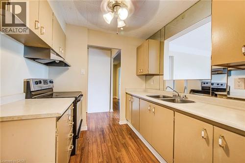 Compact kitchen featuring wood-finish flooring, light-toned cabinetry, double basin sink, and an electric range with an overhead vent - 75 Hazelglen Drive Unit# 310, Kitchener, ON 
