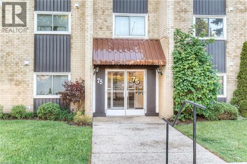 Building entrance featuring a brick facade, glass entry doors, and a corrugated metal awning - 75 Hazelglen Drive Unit# 310, Kitchener, ON 