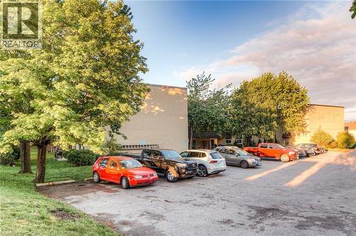 Brick exterior building with mature trees and paved parking area - 75 Hazelglen Drive Unit# 310, Kitchener, ON 