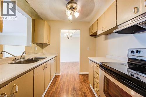 Galley kitchen featuring wood-finish flooring, light-toned cabinetry, a double basin stainless steel sink, and a black and stainless steel range with overhead ventilation - 75 Hazelglen Drive Unit# 310, Kitchener, ON 