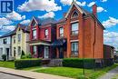 Red brick facade with a prominent arched gable, featuring black-framed windows and a covered front entry - 244 Hughson Street N, Hamilton, ON 