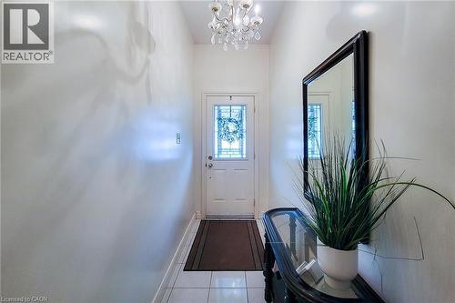 Foyer featuring a white entry door with decorative glass inserts, white tile flooring, a crystal chandelier, and a dark-framed mirror - 244 Hughson Street N, Hamilton, ON 
