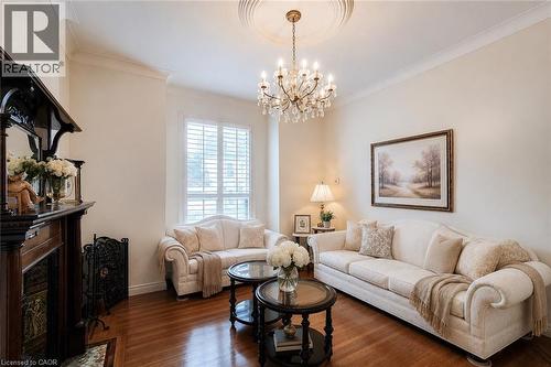 Living area featuring rich wood-finish flooring, an ornate chandelier with ceiling medallion, and crown molding - 244 Hughson Street N, Hamilton, ON 