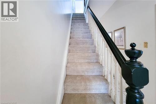 Carpeted staircase featuring a dark-toned newel post and balusters, with light-toned walls and framed artwork - 244 Hughson Street N, Hamilton, ON 