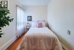 Hardwood flooring with prominent baseboards, light-colored walls, and a window with sheer curtains - 