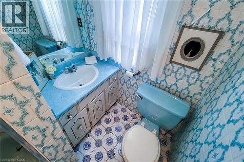 Bathroom featuring patterned blue and white wall tiles, blue vanity countertop, white sink, white window sheers, and blue toilet - 244 Hughson Street N, Hamilton, ON 