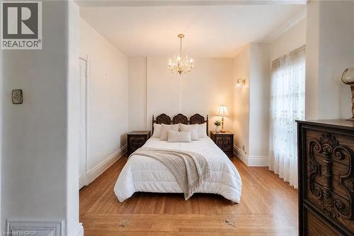 Bedroom featuring wood-finish flooring, a crystal chandelier, wall sconces, a window with sheer curtains, and detailed baseboard and crown molding - 244 Hughson Street N, Hamilton, ON 