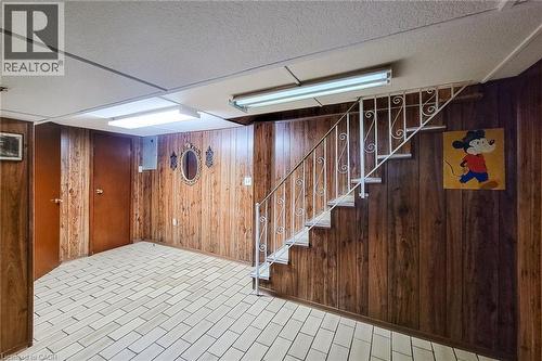 Lower level featuring wood-panel walls, white floor tiles, and a staircase with a decorative metal railing - 244 Hughson Street N, Hamilton, ON 