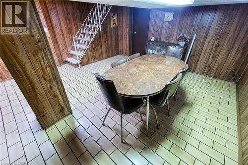 Room featuring wood-finish paneling, light-toned rectangular floor tiles, and a white metal staircase with carpeted treads - 244 Hughson Street N, Hamilton, ON 