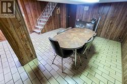 Room featuring wood-finish paneling, light-toned rectangular floor tiles, and a white metal staircase with carpeted treads - 