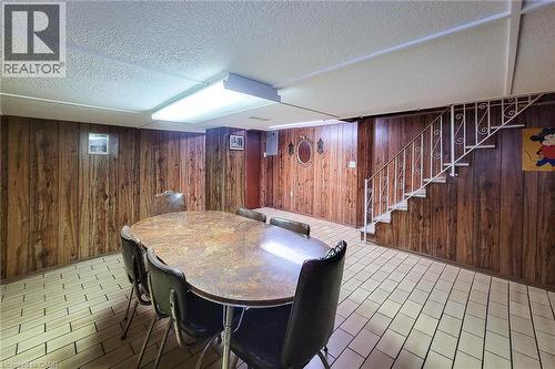 Recreation room featuring wood paneling, white ceramic tile flooring, and a straight staircase with a white metal railing - 244 Hughson Street N, Hamilton, ON 