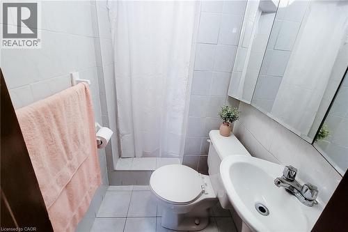 Bathroom featuring white ceramic wall tile, matching floor tile, a pedestal sink with chrome faucet, and a wall-mounted mirrored medicine cabinet - 244 Hughson Street N, Hamilton, ON 
