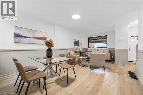 Open-concept living area featuring light wood-finish flooring, white and light grey wainscoting, a large front window, recessed lighting, and a white entry door with a frosted glass pane - 11 Ford Street, Hamilton, ON 