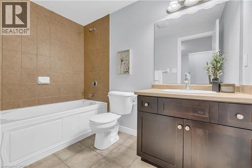 Bathroom featuring a white bathtub with a tiled surround, a toilet, a dark wood-finish vanity with a light-colored countertop, and a wall-mounted mirror - 48 Clough Crescent, Guelph, ON 