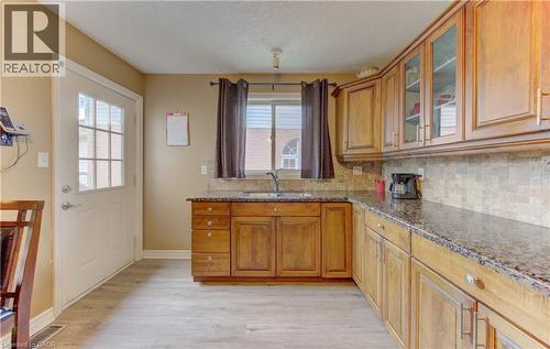Kitchen featuring wood-finish flooring, L-shaped cabinetry with glass-front uppers, granite countertops, tile backsplash, and a window above the sink - 599 Coldstream Drive, Waterloo, ON 
