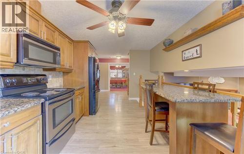 Kitchen featuring wood cabinetry, light-toned wood-finish flooring, stainless steel appliances, granite countertops, and a breakfast bar with wood paneling - 599 Coldstream Drive, Waterloo, ON 