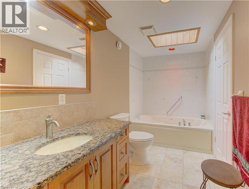 Bathroom featuring a large jetted tub, a vanity with a granite-style countertop, a single basin sink, and a framed mirror with integrated lighting - 599 Coldstream Drive, Waterloo, ON 